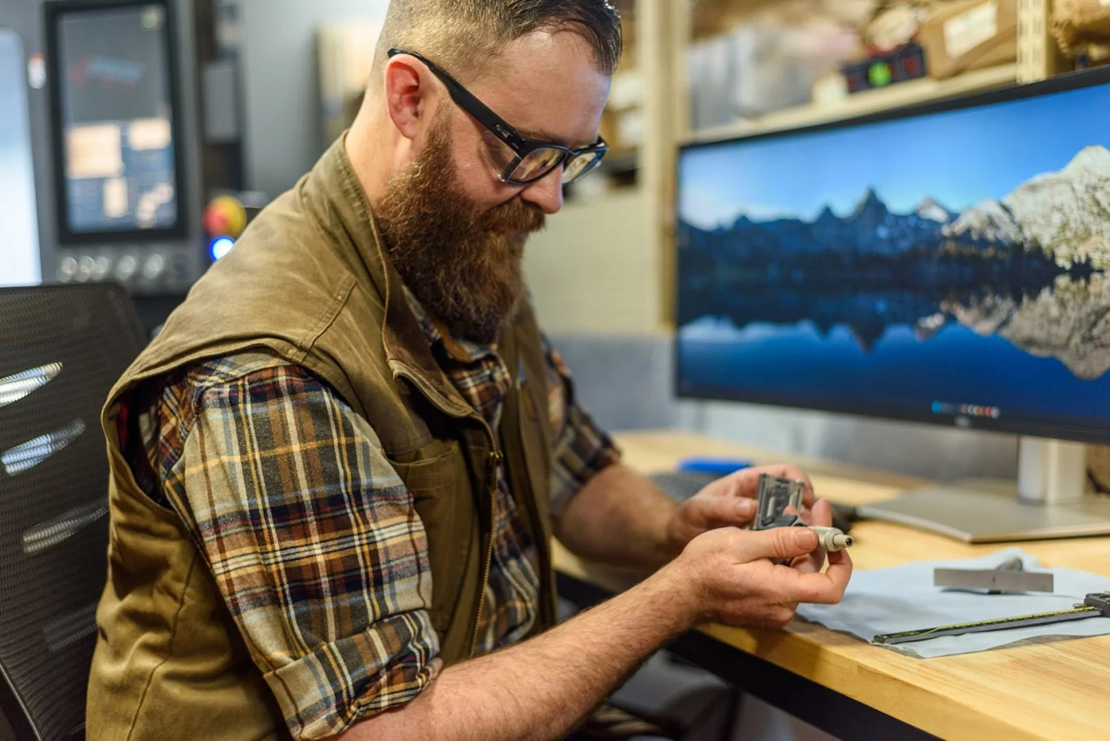 Machinist reviewing a CAD model at his desk while holding a machined part
